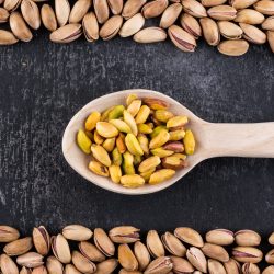 top-view-pistachios-frame-wooden-spoon-gray-texture-vertical